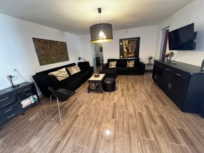 A modern living room with a black sofa, a dining table, and a TV mounted on the wall. - CASA DO PINHEIRO, near Olhos de Água River Beach and the Lake Azul (Pé de Cão)