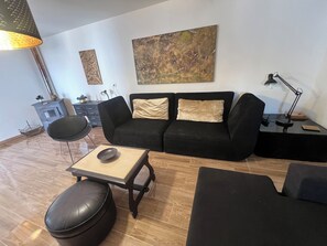A living room with a black sofa, a coffee table, a black ottoman, a lamp, and a painting on the wall. - CASA DO PINHEIRO, near Olhos de Água River Beach and the Lake Azul (Pé de Cão)