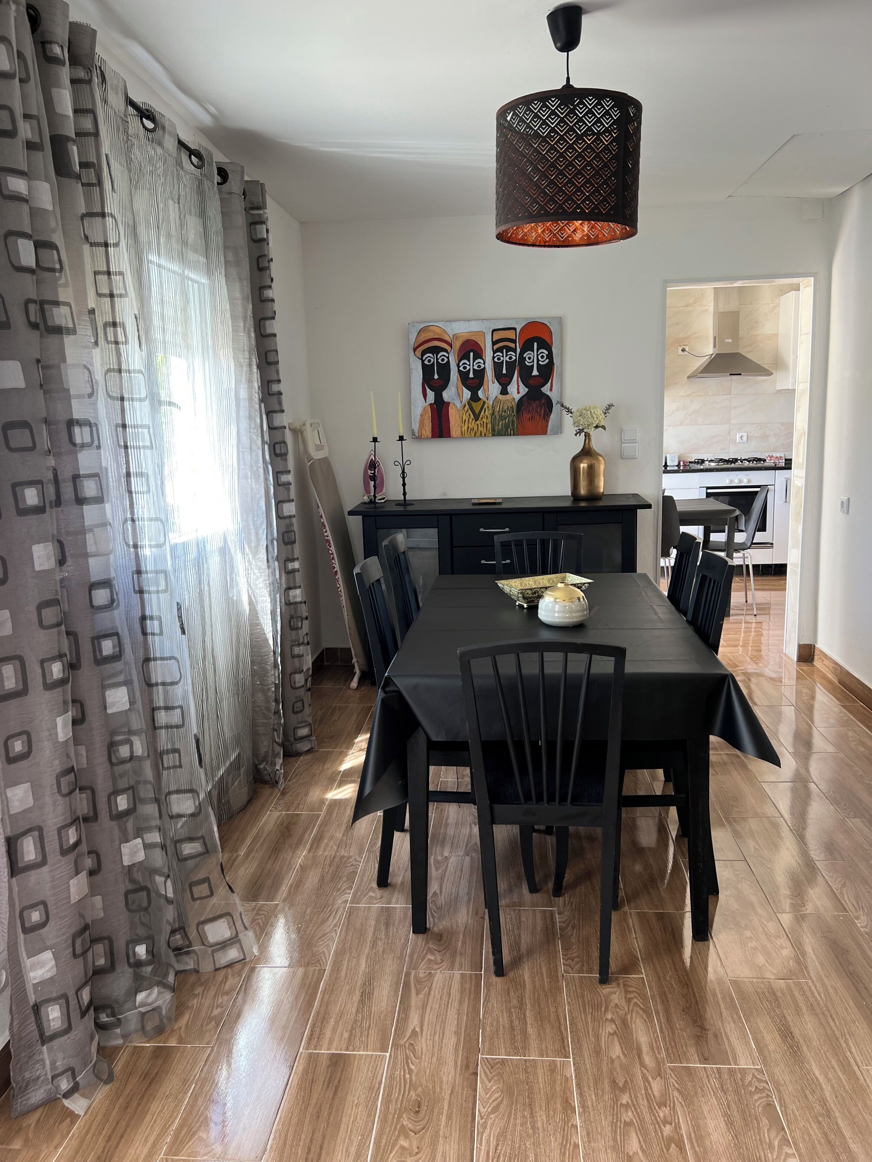 A dining area with a long table, chairs, a pendant light, and a painting on the wall.