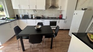 A modern kitchen with white cabinets, a black countertop, and a dining table with chairs. - CASA DO PINHEIRO, near Olhos de Água River Beach and the Lake Azul (Pé de Cão)