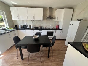A modern kitchen with white cabinets, a black countertop, and a dining table with chairs. - CASA DO PINHEIRO, near Olhos de Água River Beach and the Lake Azul (Pé de Cão)