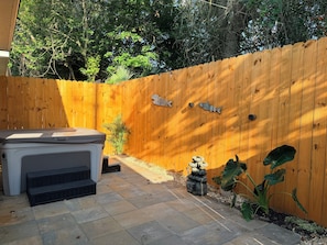 A wooden fence with decorative elements, a hot tub, and a stone sculpture in a backyard setting. - Happy Turtle NEW Renovation• Jacuzzi•Grill (Panama City Beach)