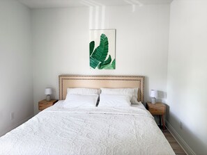 A bedroom with a large bed, two bedside tables with lamps, a wall-mounted artwork of green leaves, and a plain white wall. - Happy Turtle NEW Renovation• Jacuzzi•Grill (Panama City Beach)