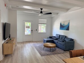 A modern living room with a flat-screen TV, a grey sectional sofa, a round wooden coffee table, and a painting on the wall. - Happy Turtle NEW Renovation• Jacuzzi•Grill (Panama City Beach)