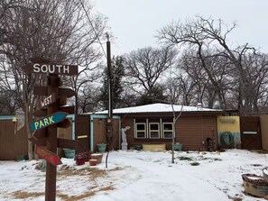 A directional signpost with 'SOUTH' and 'WEST' directions, a wooden building with a snow-covered roof, and a fenced area with potted plants.