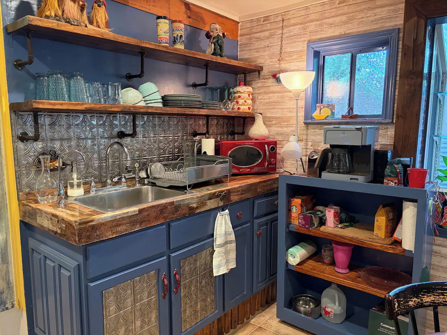Une cuisine avec des armoires bleues, un plan de travail en bois, un four à micro-ondes et divers ustensiles de cuisine.
