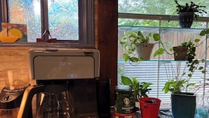 Una cafetera sobre una mesa con vistas a la ventana, una jarra de café, un paquete de Starbucks y plantas en macetas.