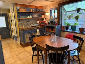 Una cocina con isla de madera, una mesa de comedor con sillas y un ventanal con plantas.