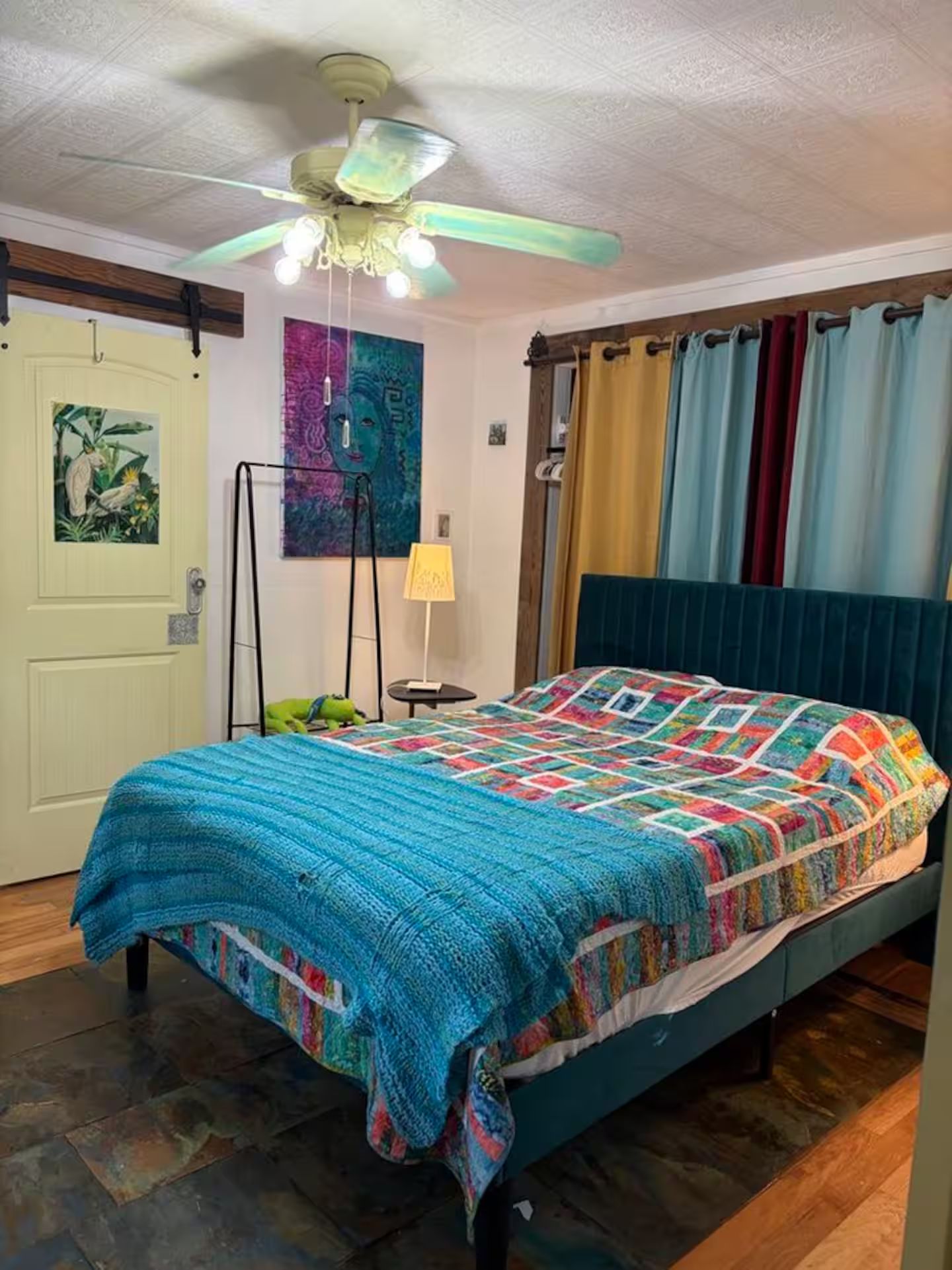 Ein Schlafzimmer mit einem Bett, einem Deckenventilator, einer Tür und einer Wand mit einem Gemälde.