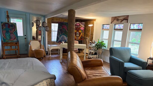 Una habitación con una cama, dos sofás, una mesa y sillas. Hay cuadros en las paredes y una ventana con vistas.