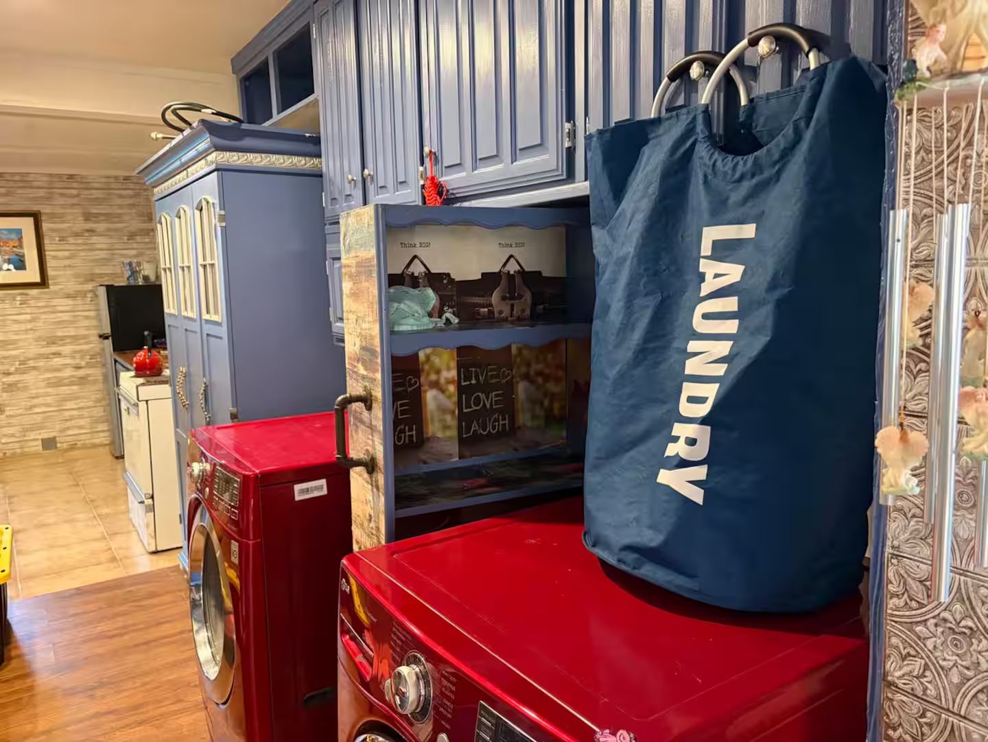 A laundry bag with 'LAUNDRY' text, a red washing machine, and a blue cabinet with a window displaying 'THINK BIG LIVE BIG'.