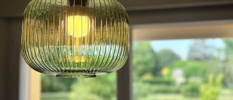 Un luminaire suspendu au design strié, une fenêtre donnant sur un paysage verdoyant et un comptoir de cuisine avec des placards.