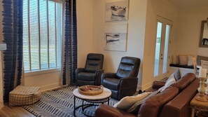 Ein Wohnzimmer mit einer Couch, zwei Sesseln, einem Couchtisch und einem Fenster mit Jalousien.
