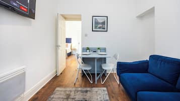 A compact living space with a dining area, a blue sofa, and a flat-screen TV mounted on the wall.