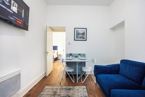 A compact living space with a dining area, a blue sofa, and a flat-screen TV mounted on the wall. - Earl's Court Residence (London)