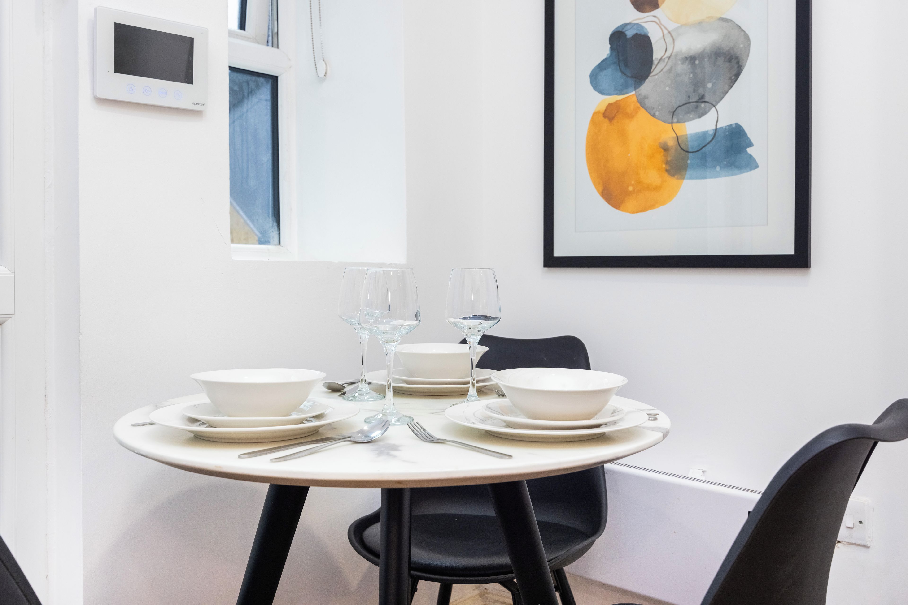 A dining table set with white plates, bowls, and cutlery, accompanied by two wine glasses.
