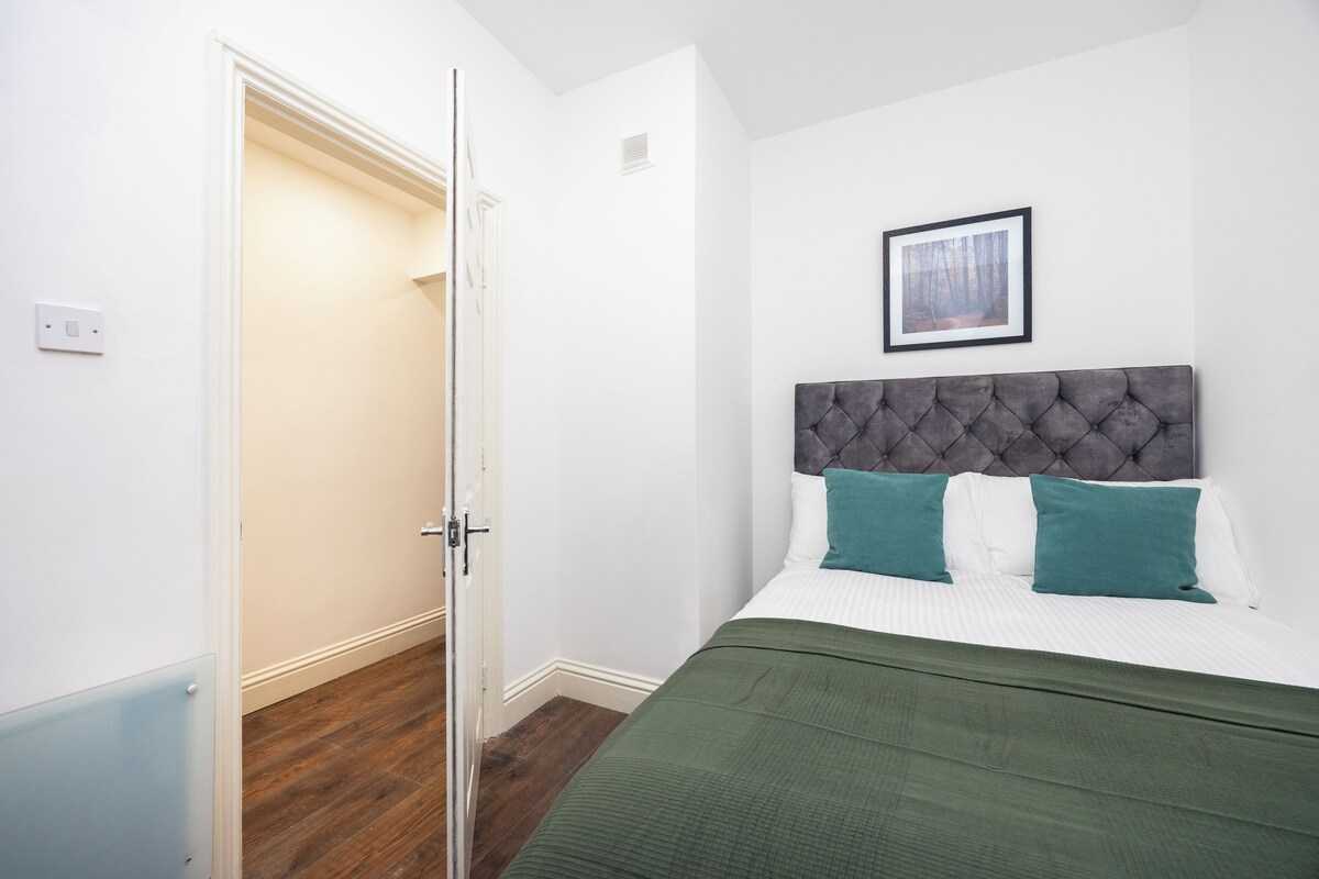 A bedroom with a bed, a headboard, a framed picture on the wall, and a partially open door.