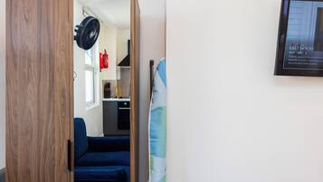 A room with a wooden wardrobe, a blue sofa, a standing fan, and a framed picture on the wall.