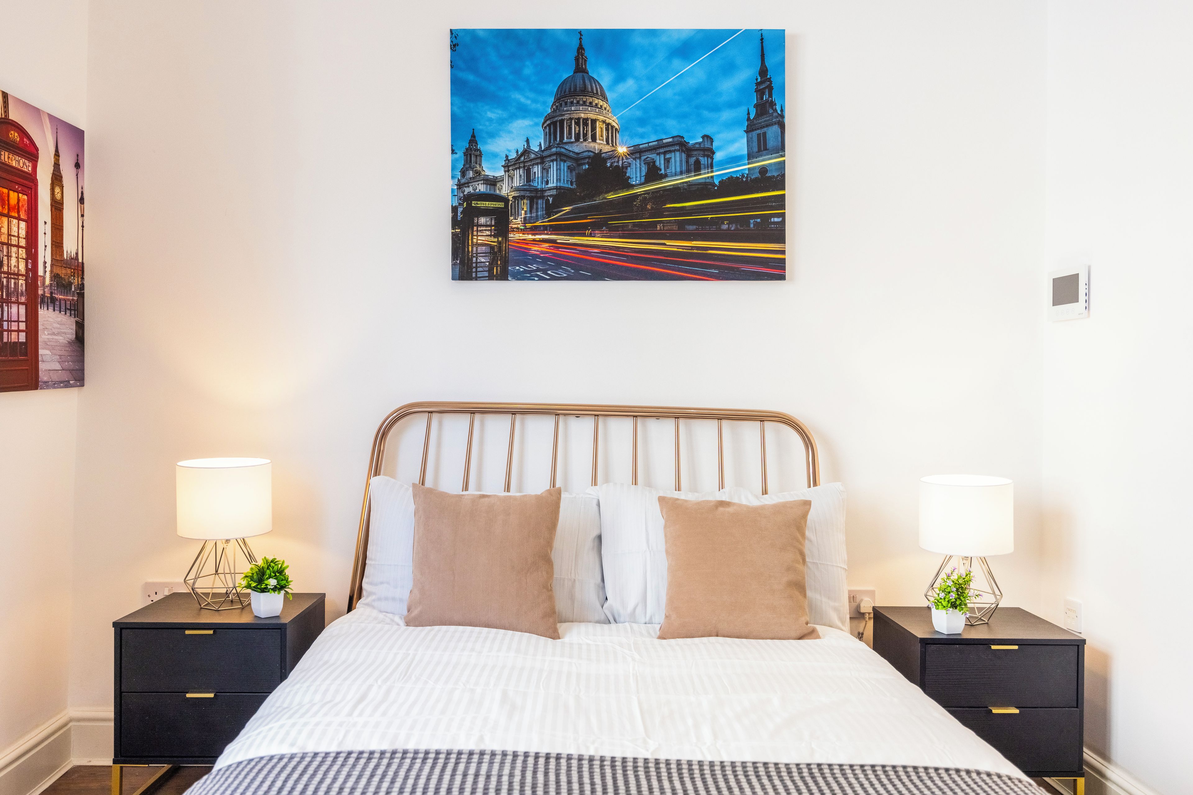 A hotel room with a large bed, two bedside tables with lamps, a wall-mounted painting of a cityscape, and a view of the street outside.