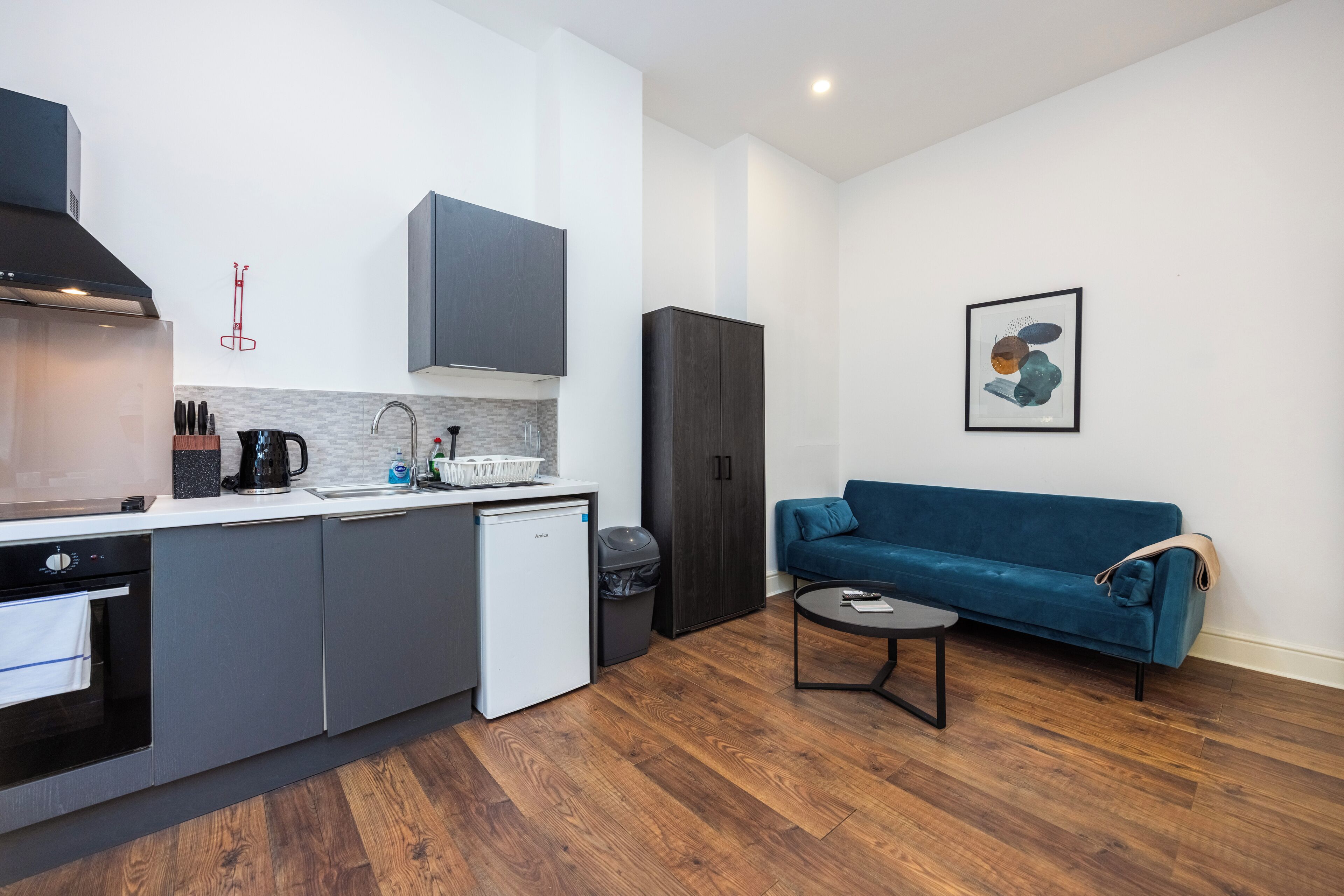 A compact living space with a kitchenette, a blue sofa, and a small dining table.