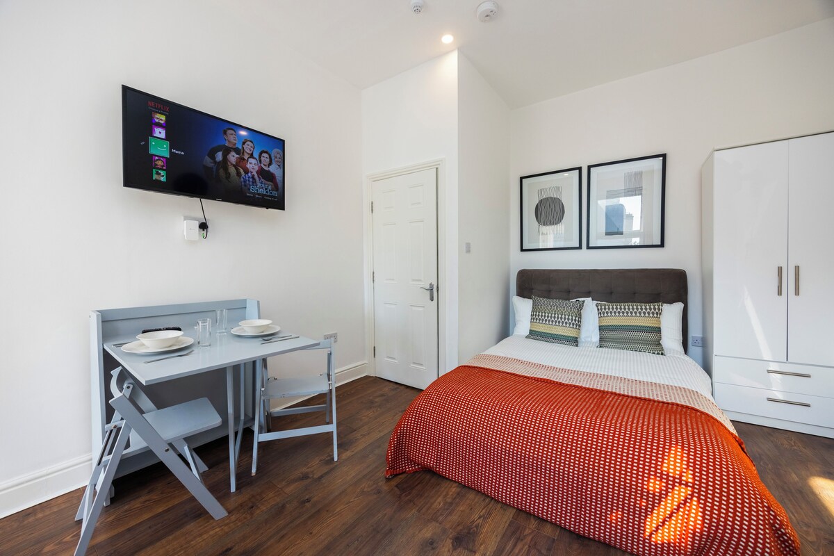 A modern bedroom with a bed, a desk, and a television mounted on the wall.