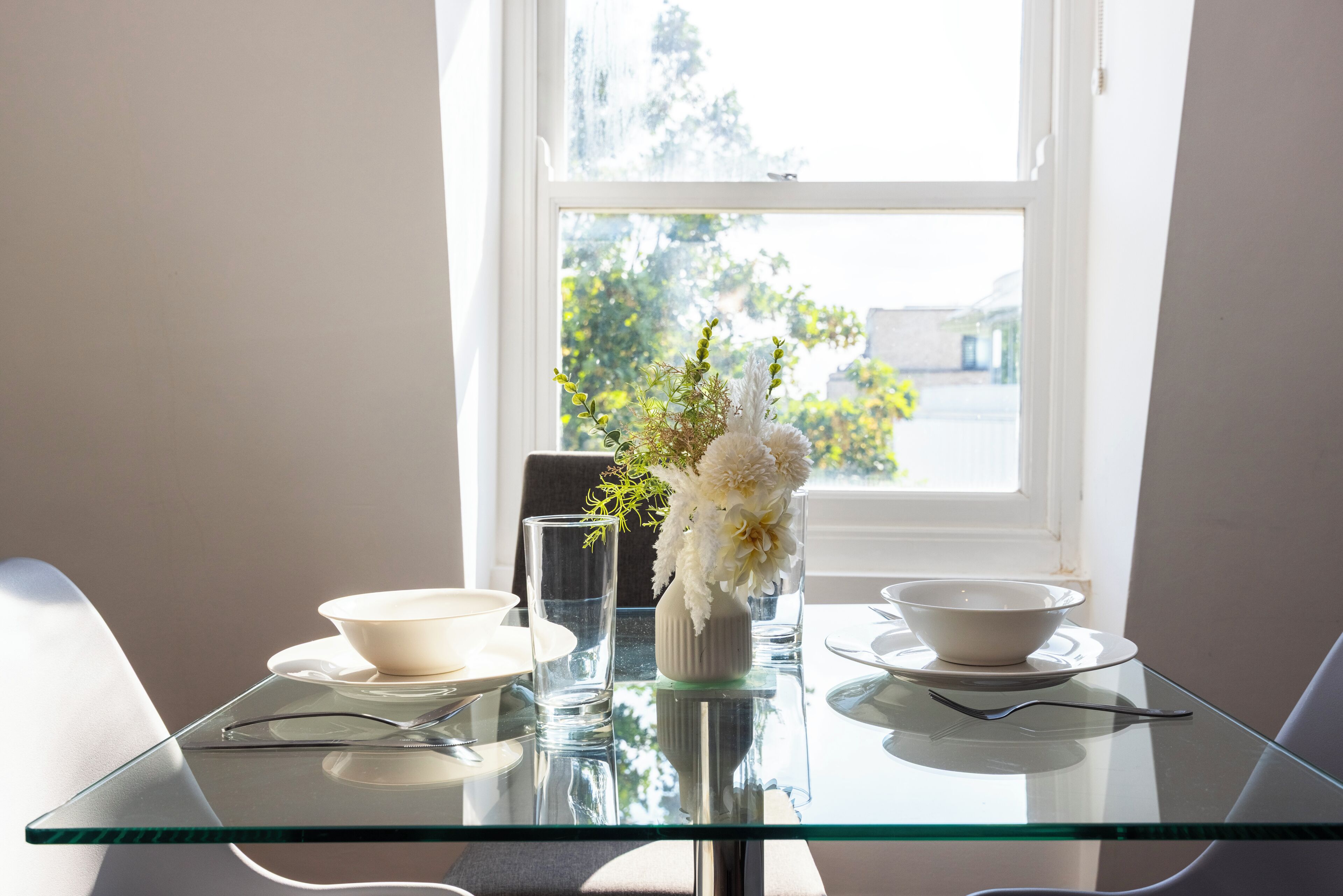 A dining table with a vase of flowers, two bowls, and cutlery.