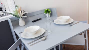 A dining table with white plates, bowls, cutlery, a remote control, and a vase with dried flowers.