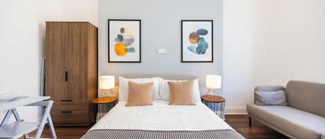 Una habitación de hotel moderna con una cama, un sofá, un escritorio y un armario. Hay dos cuadros en la pared.
