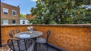 A patio with a round table and four chairs, a brick wall, and a tree in the background.