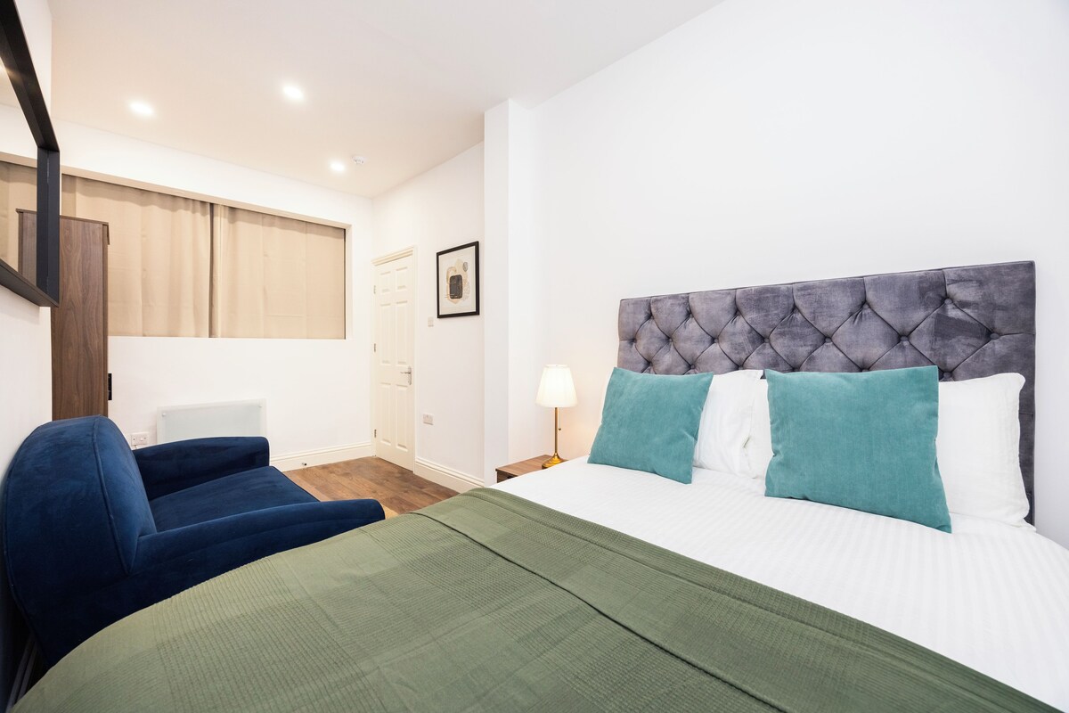 A hotel room with a bed, a chair, a nightstand, and a window with curtains.