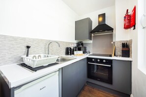 A compact kitchen with a dishwasher, stove, and a microwave. - Earl's Court Residence (London)