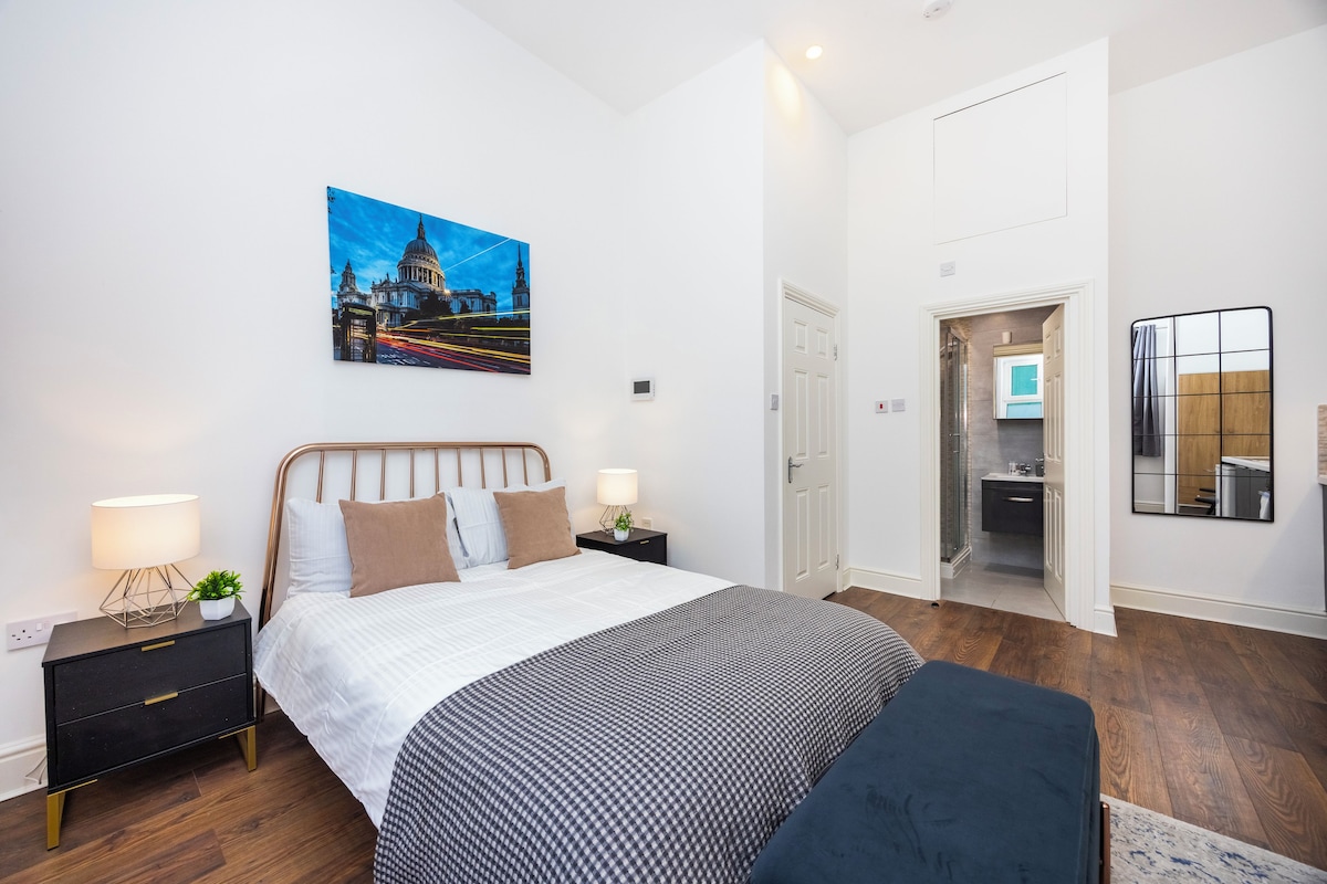A modern bedroom with a large bed, bedside tables, a nightstand, a wall-mounted mirror, and a door leading to a bathroom.