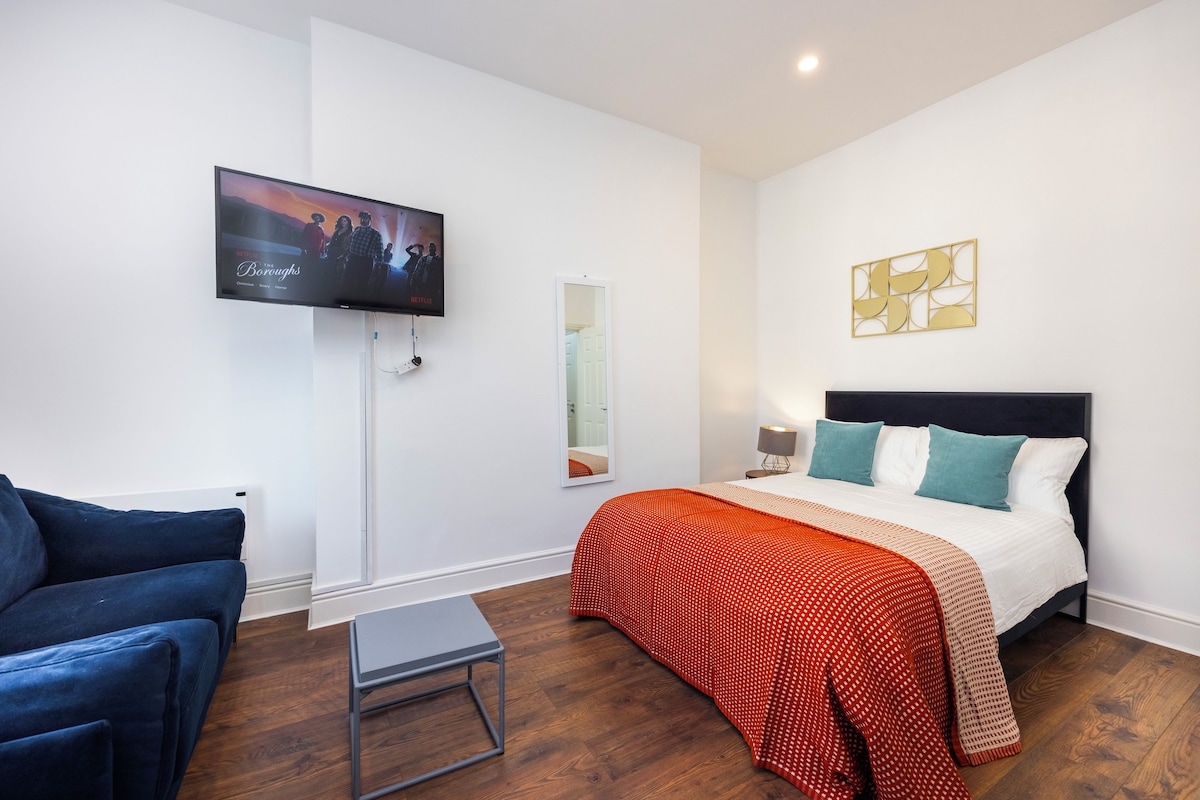A modern bedroom with a bed, a TV mounted on the wall, a small table, and a blue chair.