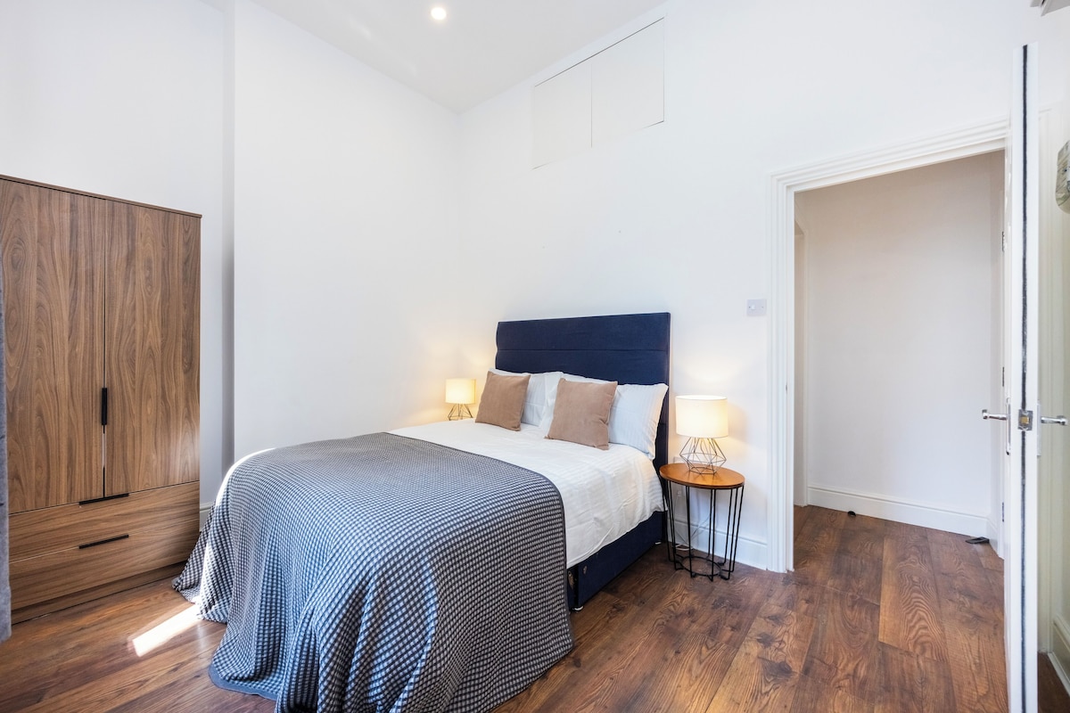 A bedroom with a bed, bedside tables, a wardrobe, and a door leading to another room.