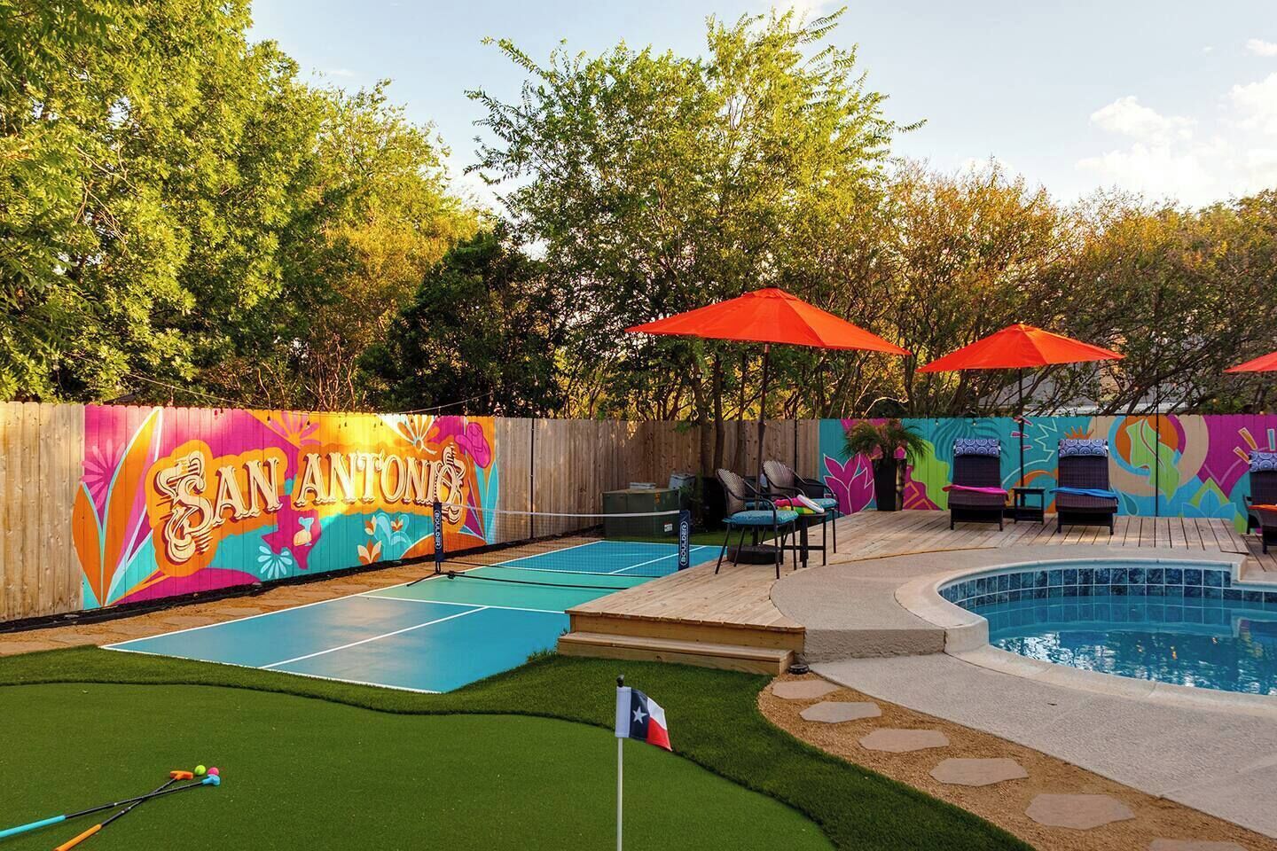 Un jardin avec un court de tennis, une piscine et une fresque peinte sur le mur de clôture.
