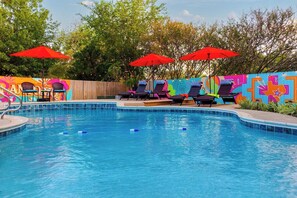 A swimming pool with lounge chairs and red umbrellas, surrounded by a colorful mural. - NEW! Pool, HotTub, Pickleball, Mini Golf + Theater (San Antonio)