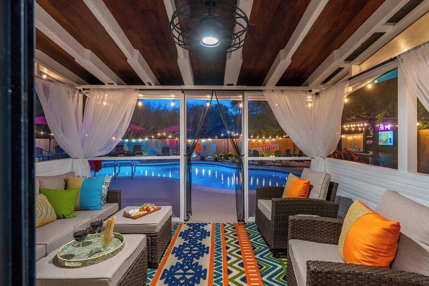 A poolside area with wicker furniture, a glass table with a tray, and a view of the pool and outdoor seating area.