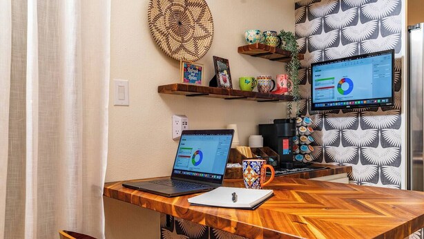 Ett skrivbord i trä med två bärbara datorer, en kaffemaskin och en mugg.