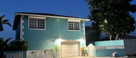 A two-story house with a garage, a fenced yard, and a tree.