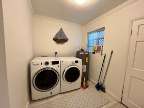 A laundry room with two front-loading washing machines, a broom, and a window with a view. - Waterfront Home 3BR - Swim & Snorkel from Patio (Nassau)