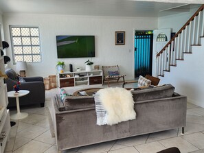 A living room with a grey sofa, a television, a staircase, and a window with a view. - Waterfront Home 3BR - Swim & Snorkel from Patio (Nassau)