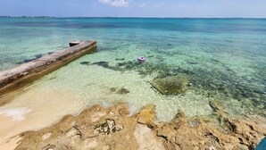 A clear beach with a rocky foreground and a wooden pier extending into the turquoise sea. - Waterfront Home 3BR - Swim & Snorkel from Patio (Nassau)