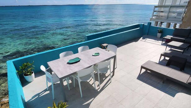 An outdoor patio with a table and chairs, a seating area with a bench, and a view of the ocean. - Waterfront Home 3BR - Swim & Snorkel from Patio (Nassau)