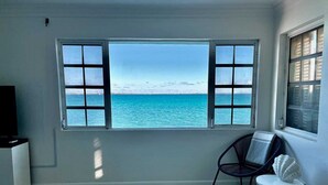 A room with a large window offering a view of the sea, a chair, a small round table, and a television on a stand. - Waterfront Home 3BR - Swim & Snorkel from Patio (Nassau)