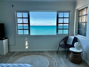 A room with a large window offering a view of the sea, a chair, a small round table, and a television on a stand. - Waterfront Home 3BR - Swim & Snorkel from Patio (Nassau)