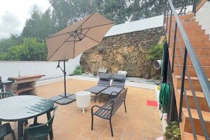 An outdoor patio with a table, chairs, a lounge area with cushions, and a large umbrella. - Charming 3-bedroom House Rental in Trofa, Portugal (Trofa)