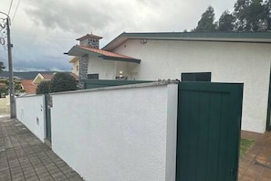 A white building with a green gate, a red-roofed tower, and a paved walkway. - Charming 3-bedroom House Rental in Trofa, Portugal (Trofa)