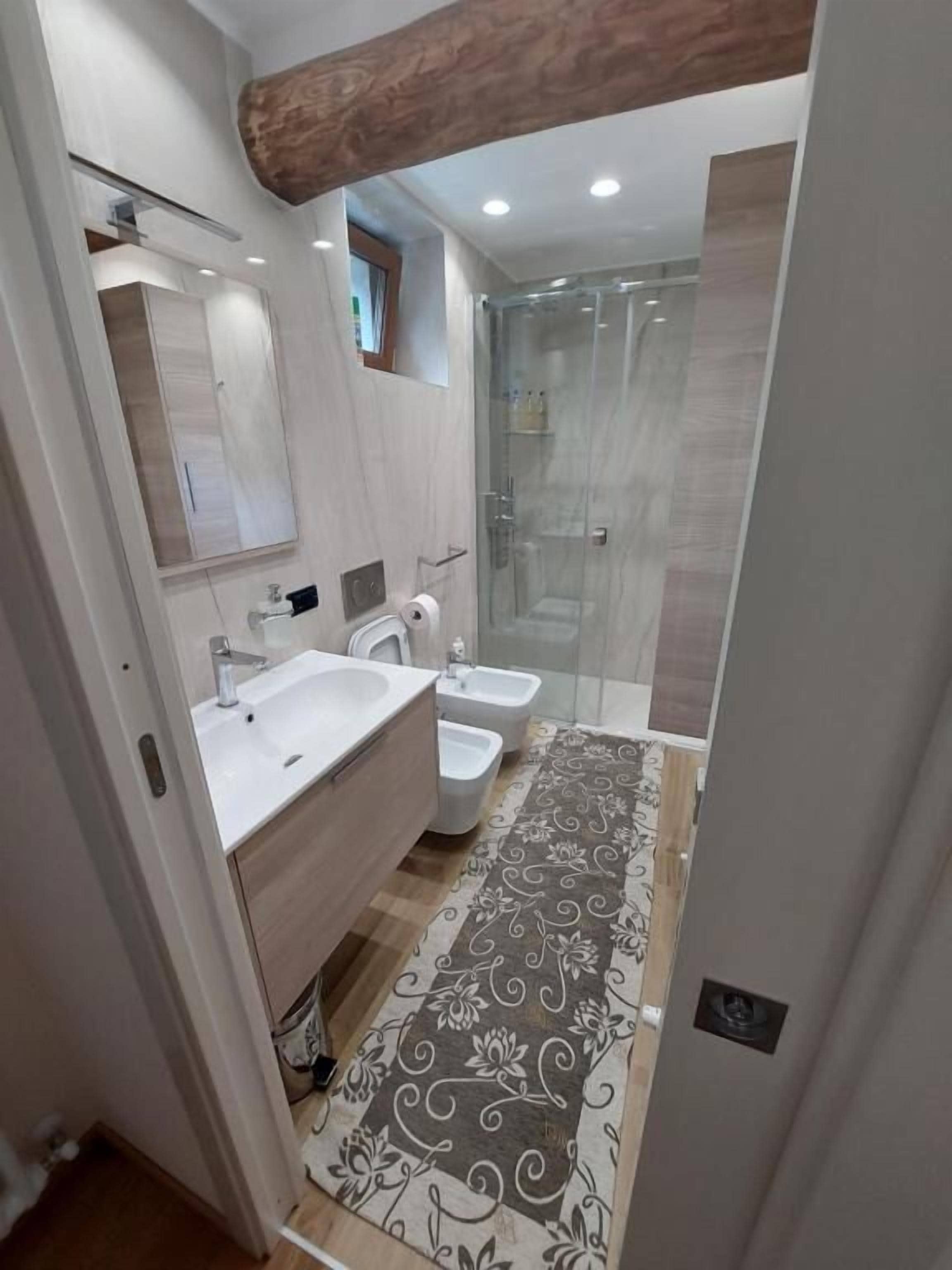 Un baño moderno con un espejo grande, dos lavamanos, ducha y un tapete estampado.