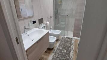 Un baño moderno con un espejo grande, dos lavamanos, ducha y un tapete estampado.