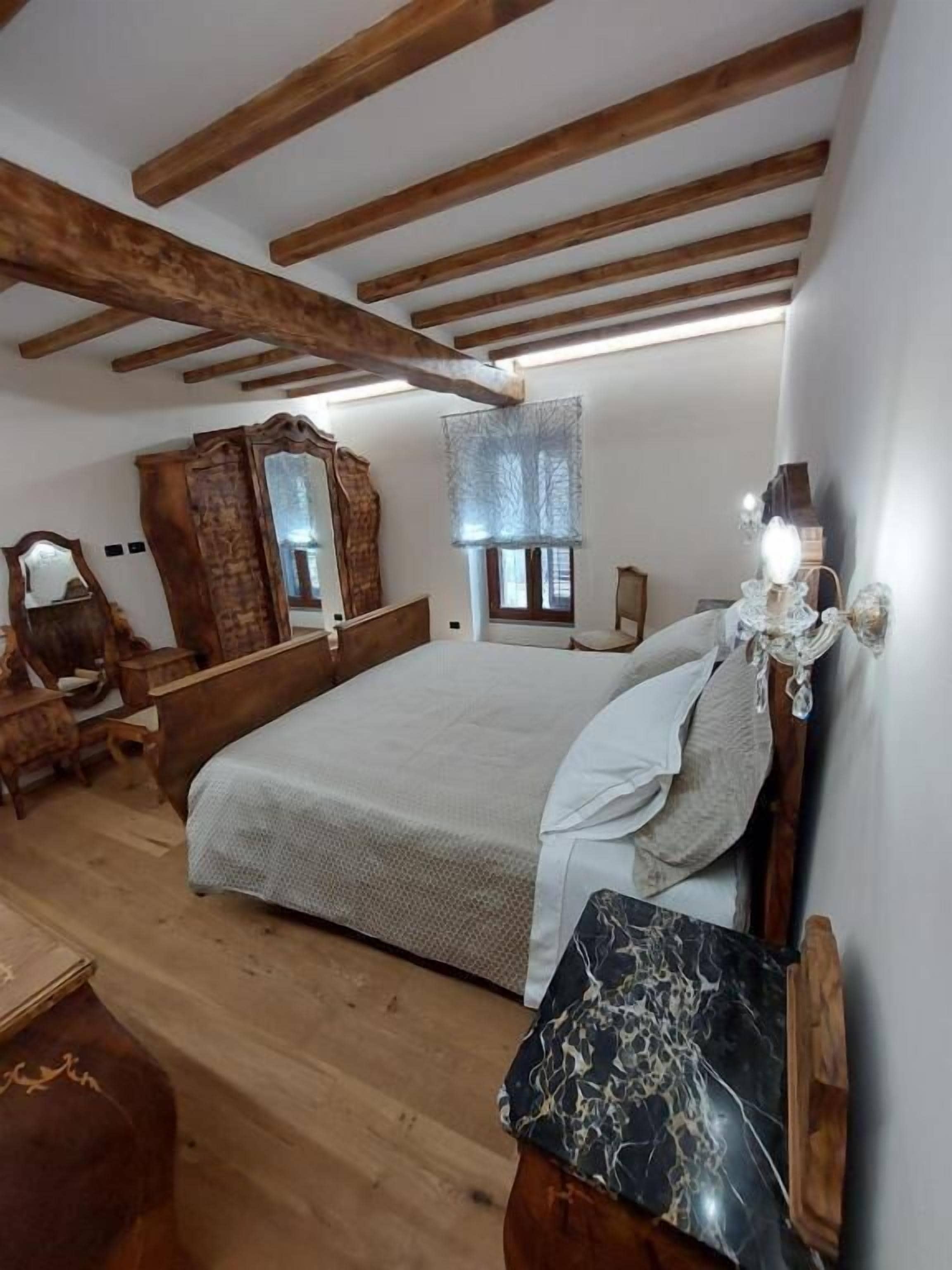 Un dormitorio con una cama de madera, una mesita de noche, un espejo y una ventana con persianas.